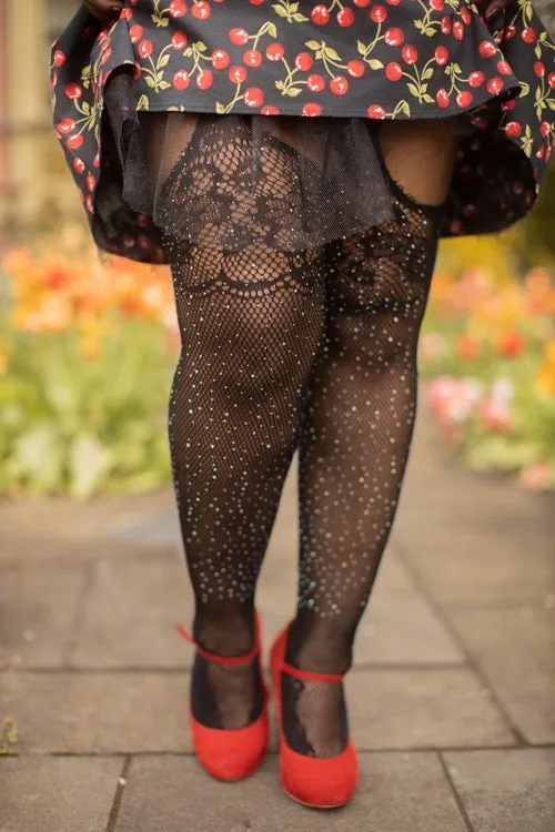 A person stands outdoors on a paved path wearing a black skirt with red cherry print, sheer black lace fishnet tights with…