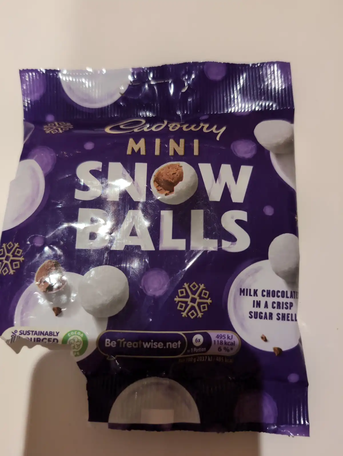 A close-up of a purple Cadbury Mini Snow Balls candy package, showing the product name and 'milk chocolate in a crisp sugar…
