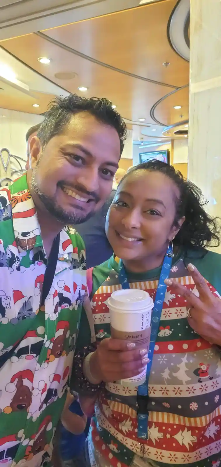 A selfie of a smiling man and woman in festive holiday-themed clothing, both wearing Christmas sweaters with cartoon animals…