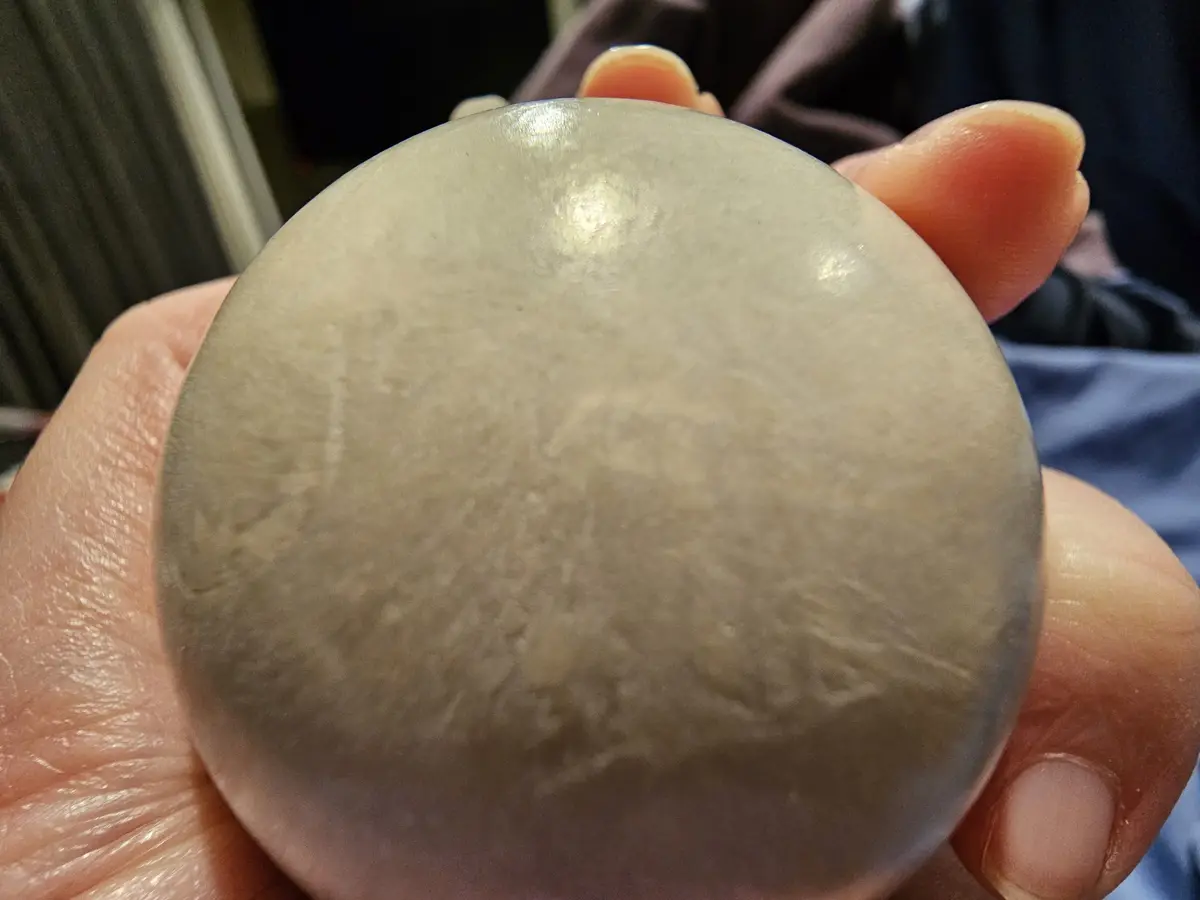 A close-up photo shows a hand holding a smooth, translucent, grayish sphere that resembles a crystal ball. The surface has…