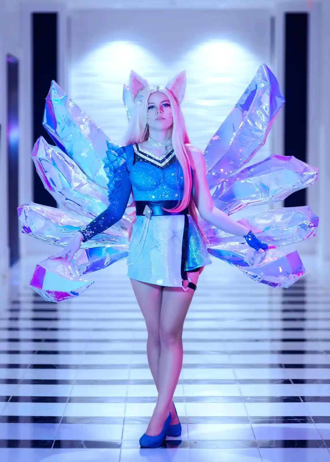 A person in a detailed cosplay of a nine-tailed fox character, featuring large, iridescent crystal-like wings, cat ears, and…