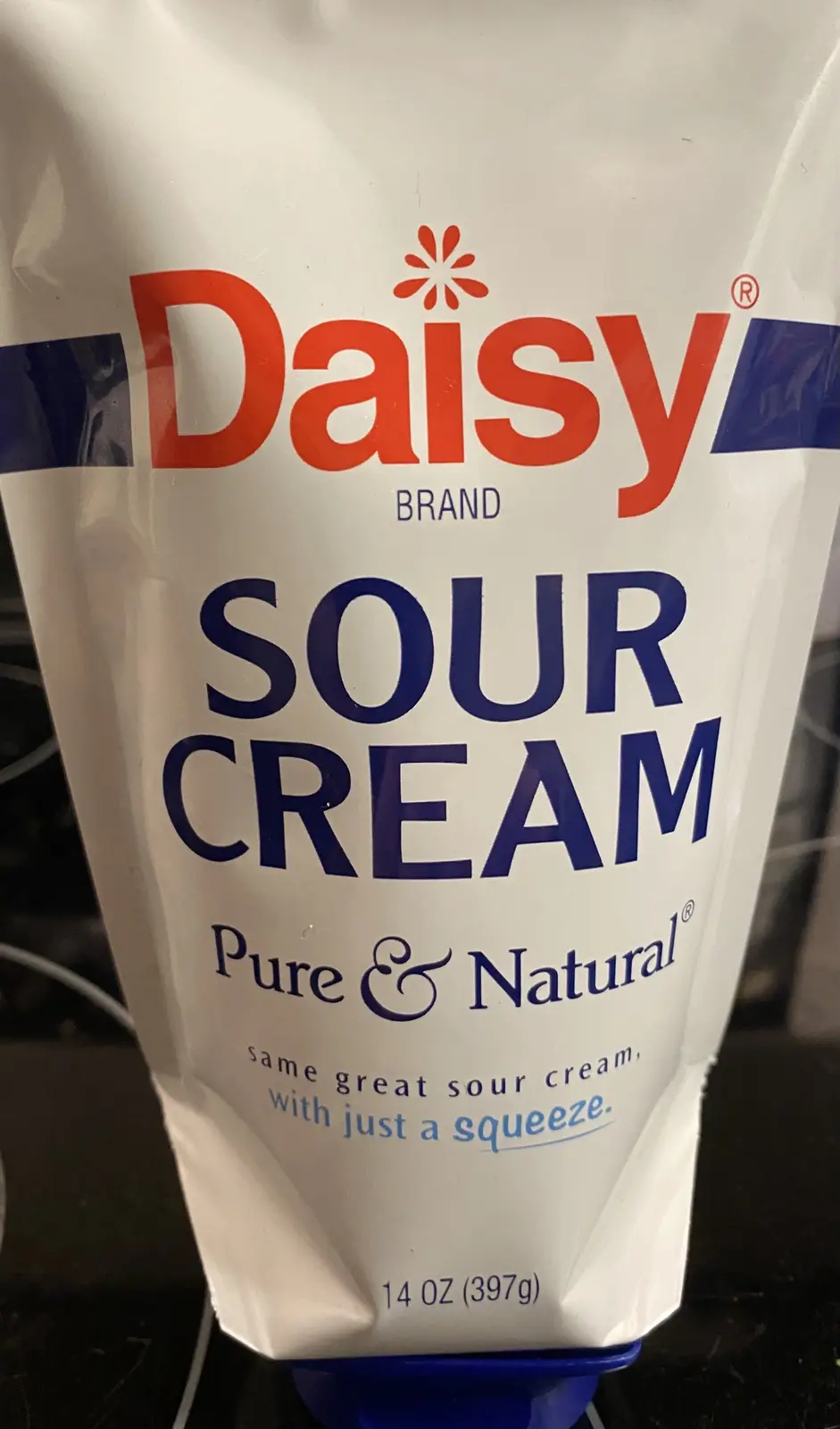 A close-up of a Daisy Brand sour cream squeeze pouch, showing the brand name, product type, and tagline 'same great sour…