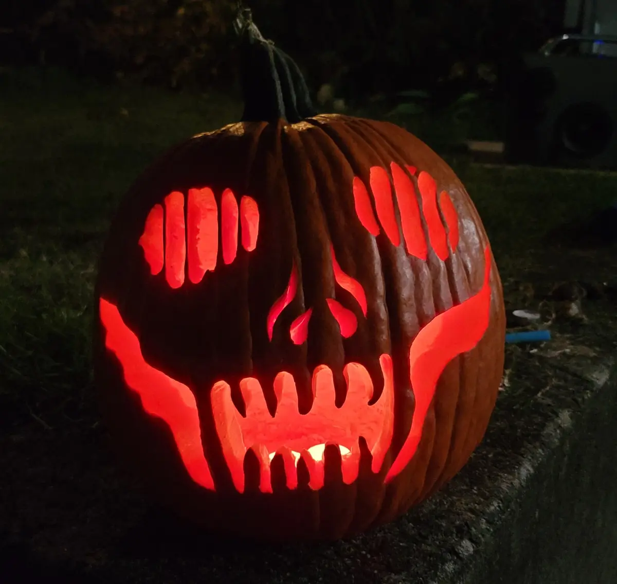 A carved Halloween pumpkin with a menacing face, featuring glowing red eyes, sharp teeth, and flame-like markings, sits on a…