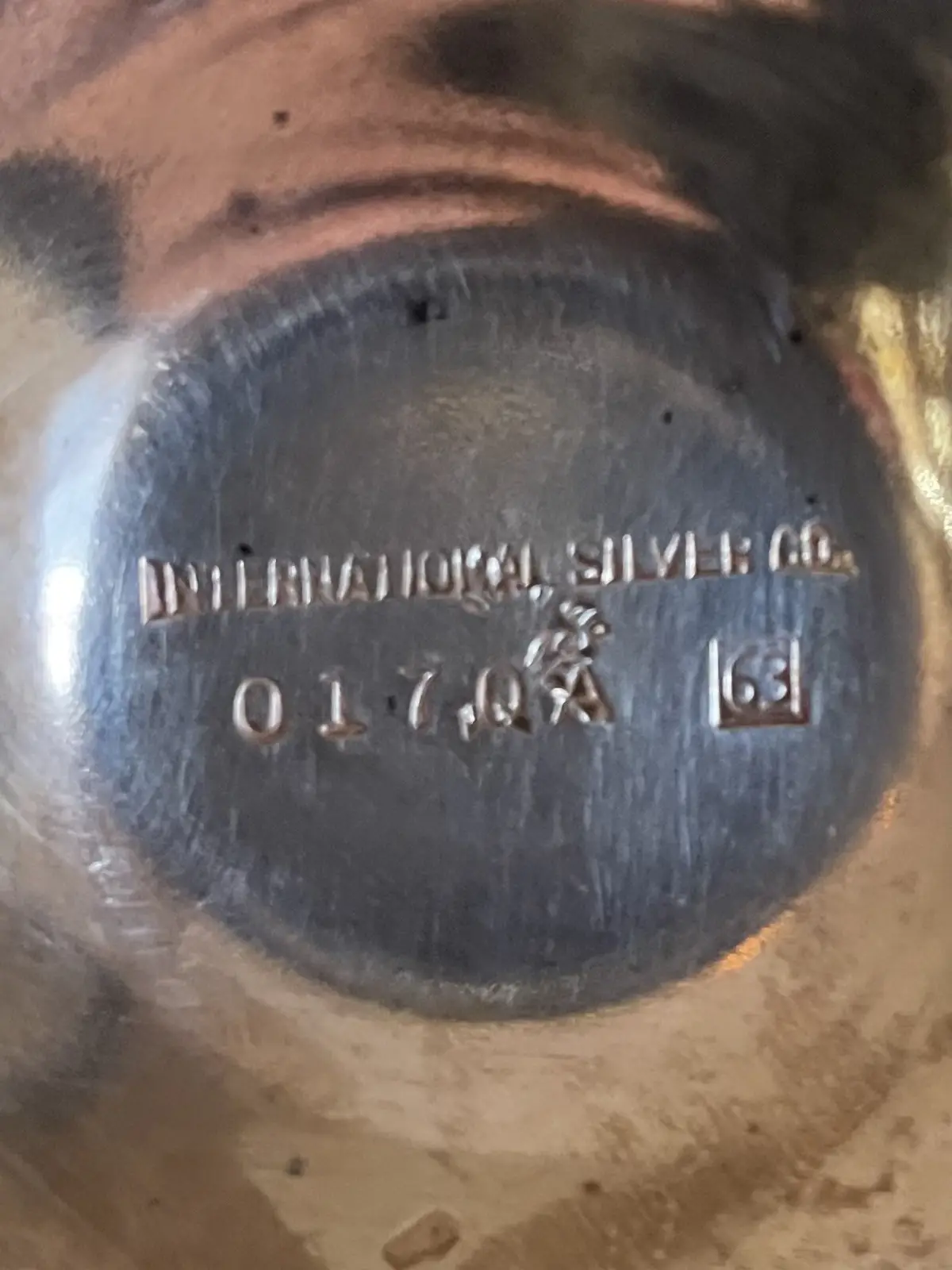 A close-up of a tarnished silver item's bottom, showing an embossed maker's mark reading 'INTERNATIONAL SILVER CO.' and a…