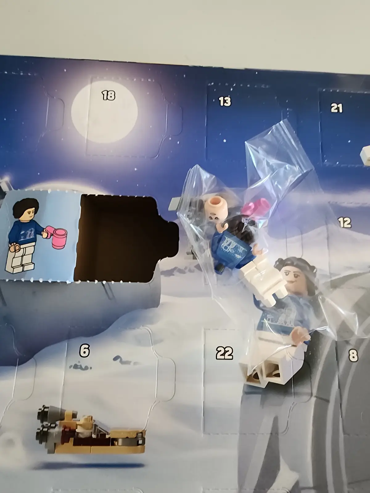 A close-up of a LEGO Star Wars Advent Calendar with several numbered compartments open, revealing spilled contents including…