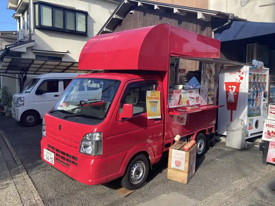 A bright red Japanese food truck parked on a street, its side serving window open with menus for items like mochi ice cream…