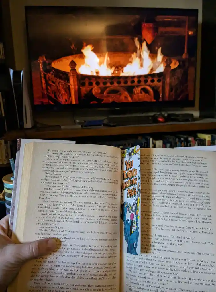 A person holds an open book with visible text, featuring a colorful bookmark that reads 'You TURNED ANOTHER PAGE!' in bold…