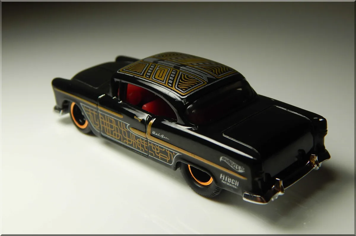 A black Hot Wheels toy car with intricate gold and silver geometric patterns on its roof and sides, red interior, and…