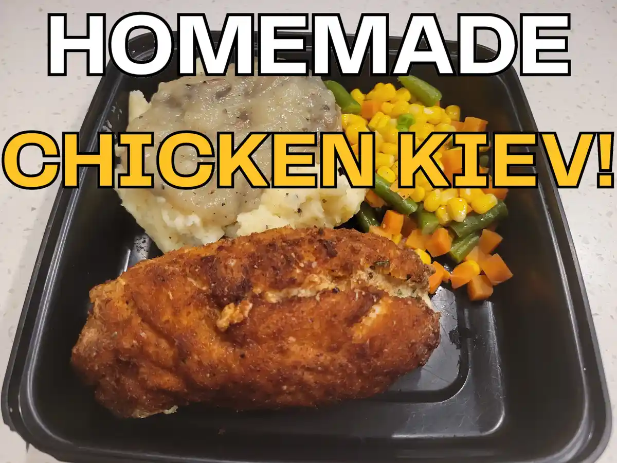 A black takeout-style tray holds a breaded chicken kiev, mashed potatoes with gravy, and mixed vegetables including corn…