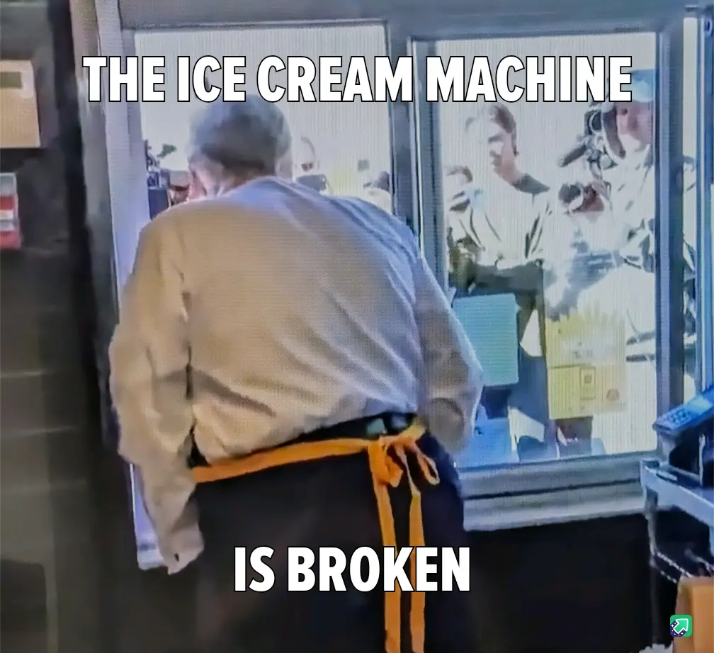 A person wearing a beige shirt and orange apron stands with their back to the camera, facing a glass-fronted ice cream…