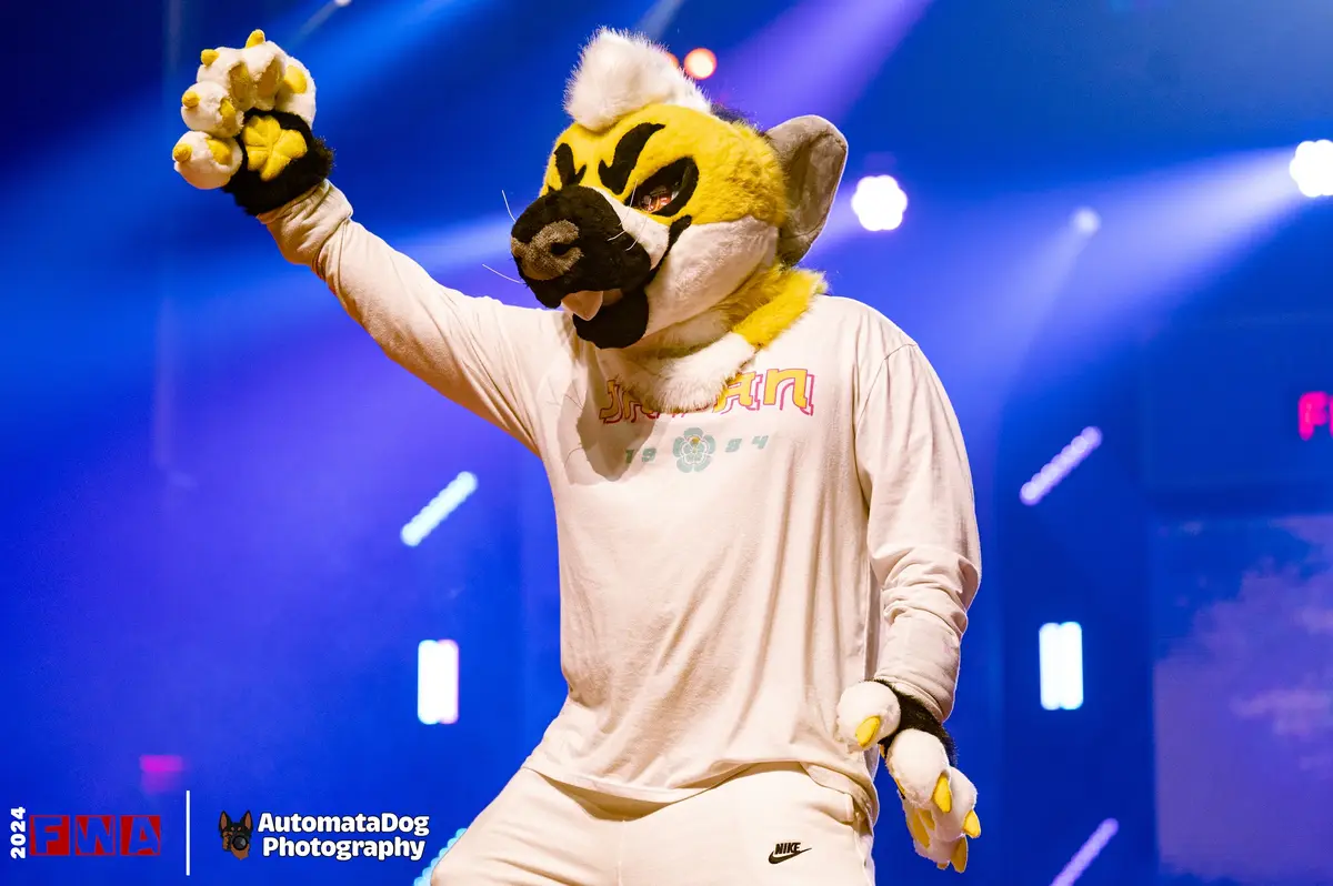 A person in a yellow and white fursuit resembling a canine or fox-like creature, wearing a white t-shirt and white Nike…