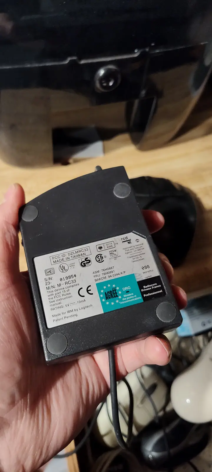 A hand holds a black Logitech computer mouse adapter with a visible label showing 'Made for IBM by Logitech' and various…