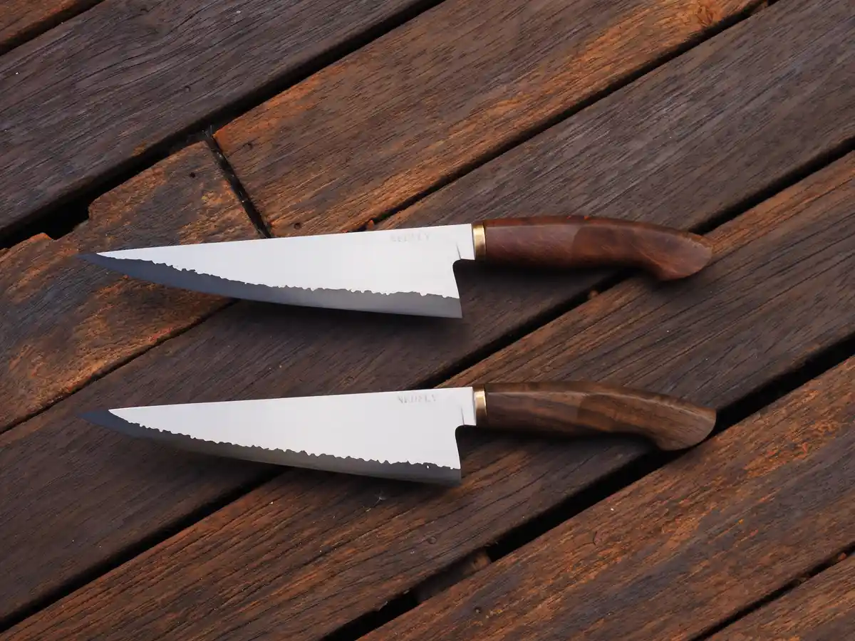 Two identical serrated knives with wooden handles and 'NEDELY' engraved on the blade lie parallel on a weathered wooden…