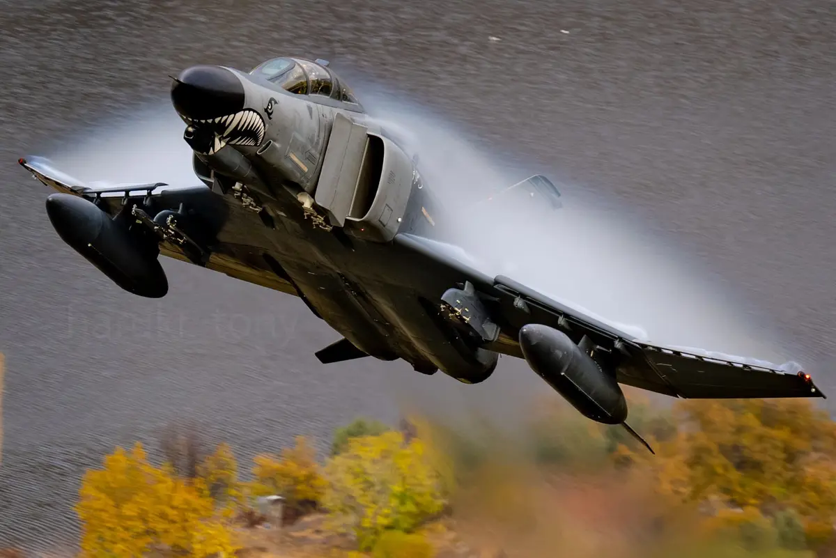 A gray military fighter jet, identifiable as an A-10 Thunderbolt II, is captured in mid-flight, banking sharply over a body…