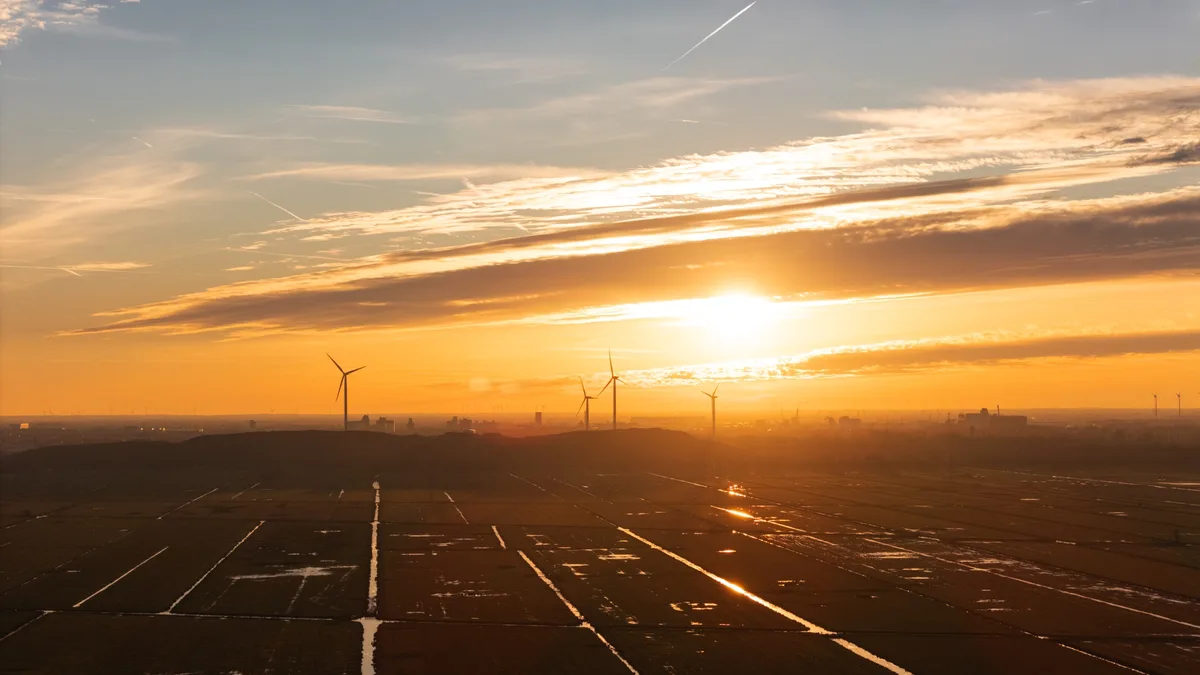 A scenic sunset over a field with wind turbines silhouetted against the orange sky, with text overlaid that reads 'i'm not…