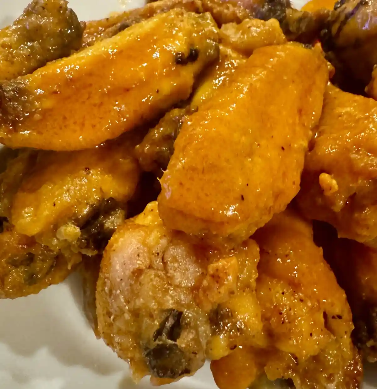 A close-up photo of several chicken wings covered in a glossy, orange cheese sauce, piled on a white plate. The text…
