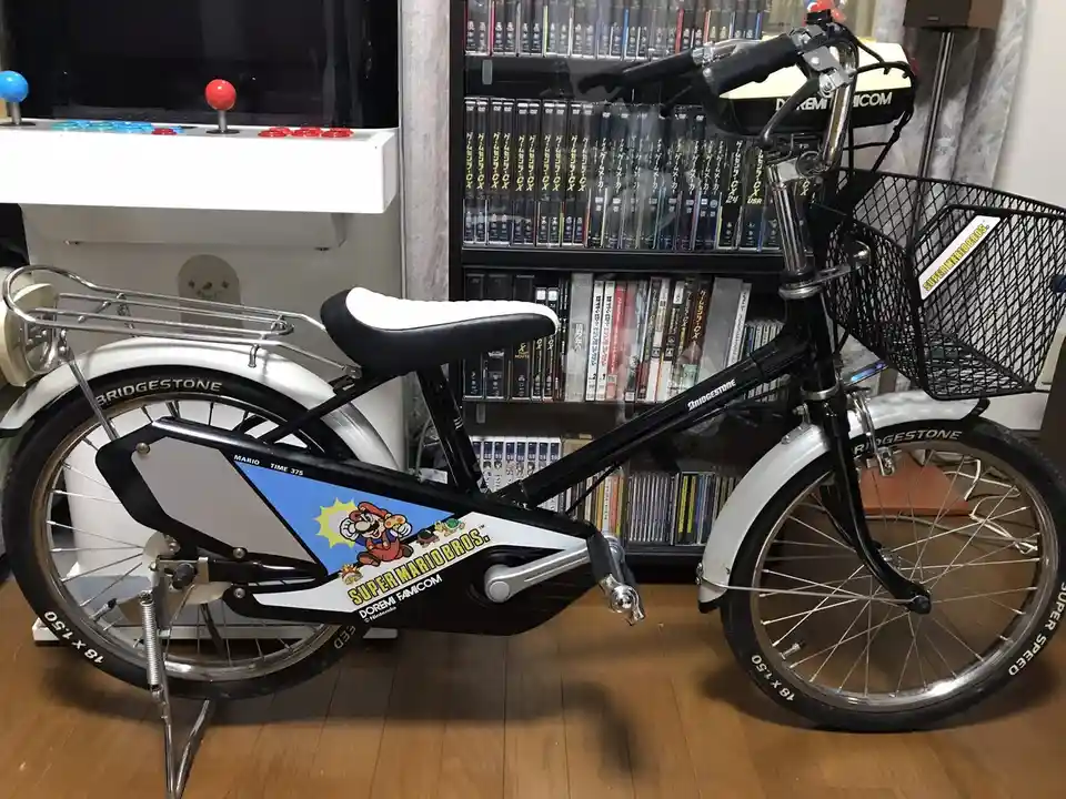 A black and white bicycle with 'Super Mario Bros.' branding and a cartoon Mario graphic on the frame, parked indoors next to…