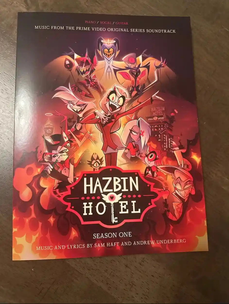 A physical copy of the 'Hazbin Hotel: Season One' piano/vocal/guitar soundtrack book, featuring artwork of multiple animated…