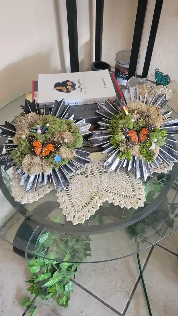 A glass-top table holds two decorative, spiky, mossy arrangements resembling hedgehogs, each adorned with orange…