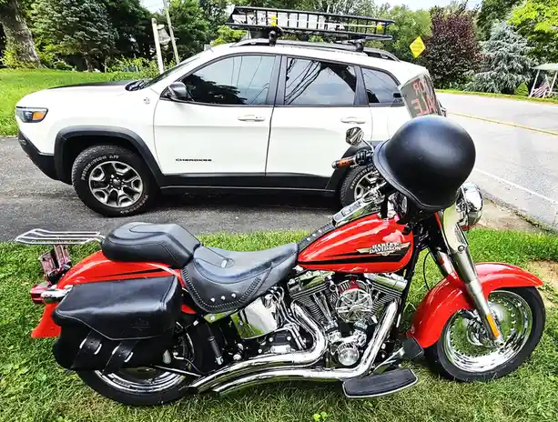 A red Harley-Davidson motorcycle with a black helmet resting on its handlebars is parked on grass in front of a white Jeep…