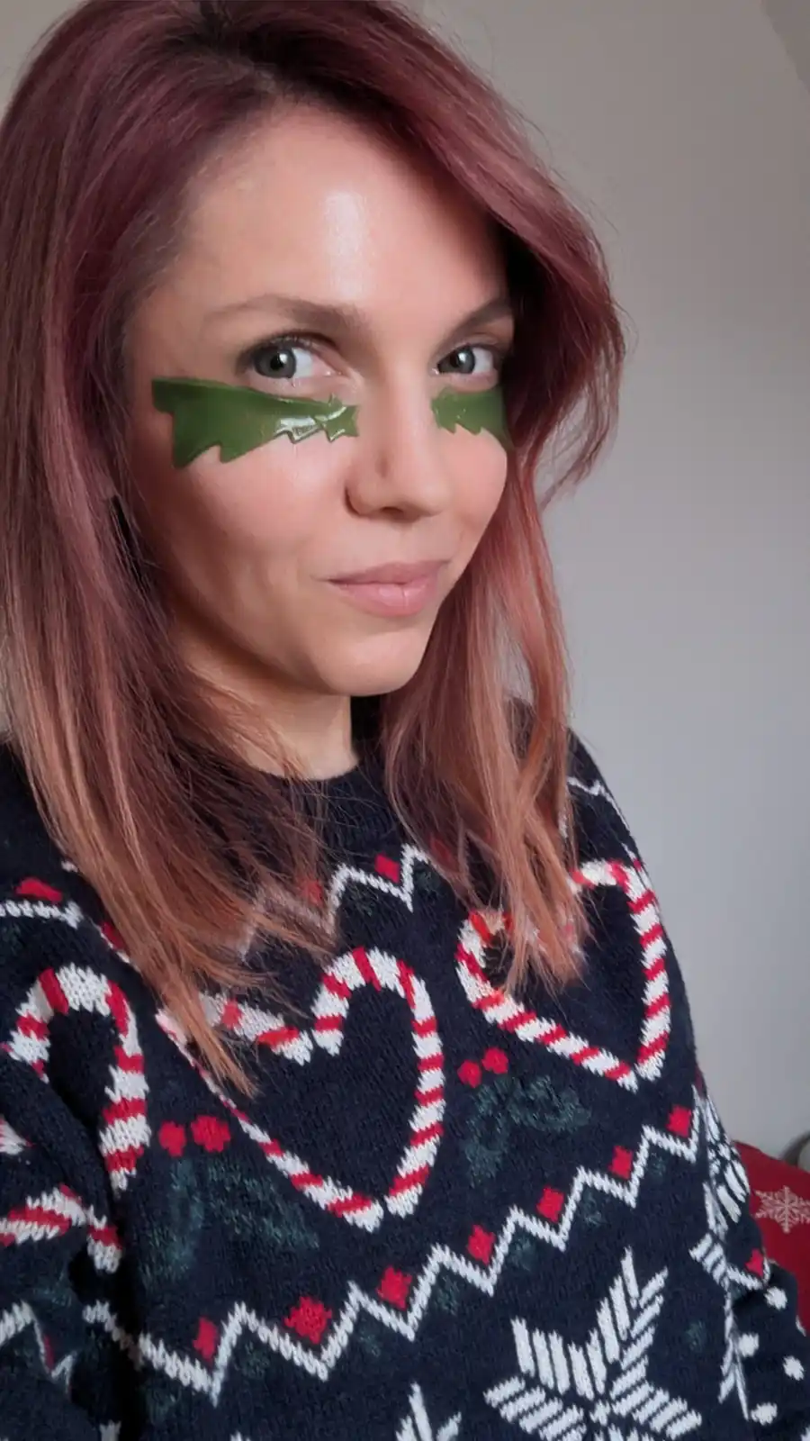 A person with reddish-brown hair wears a festive Christmas sweater with candy cane and snowflake patterns, while green…