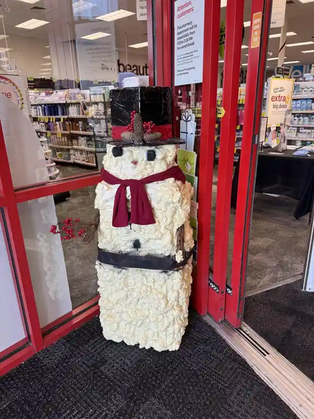 A snowman decoration made entirely of popcorn kernels stands in the doorway of a retail store, wearing a black top hat with…