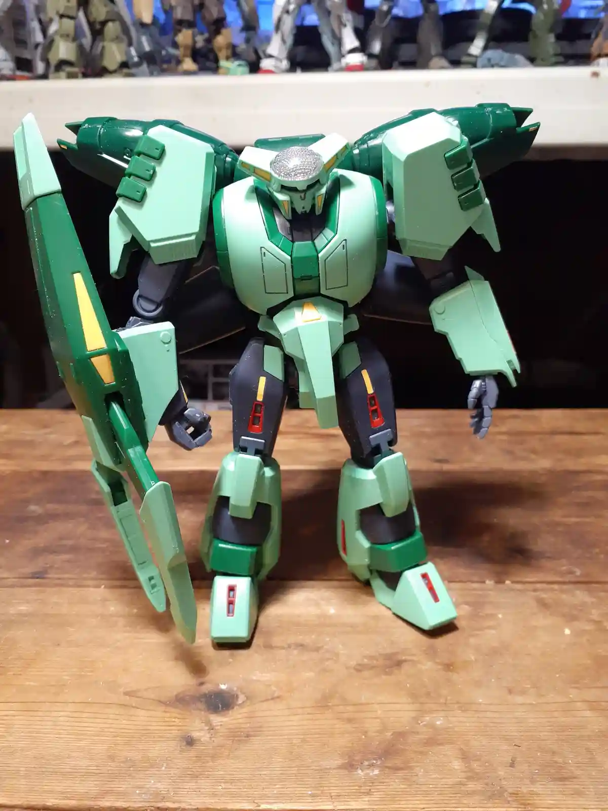 A green and black plastic robot model stands on a wooden surface, holding a large green weapon. The background shows other…