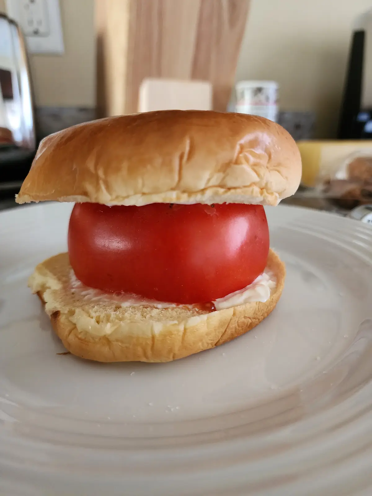 A close-up photo shows a simple sandwich made with a single large red tomato placed between two halves of a soft…