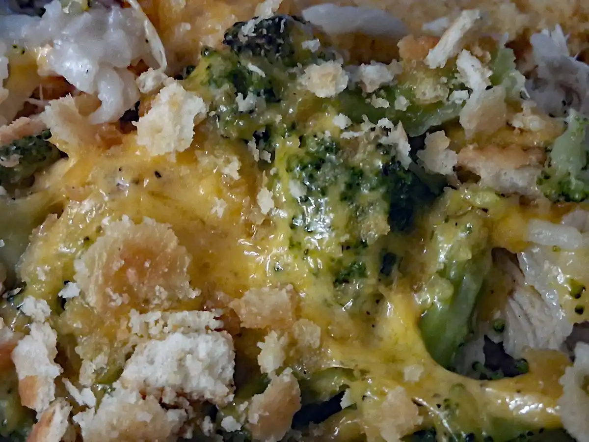 A close-up photo of a cheesy broccoli casserole with melted orange cheese, green broccoli florets, and a golden-brown crumb…