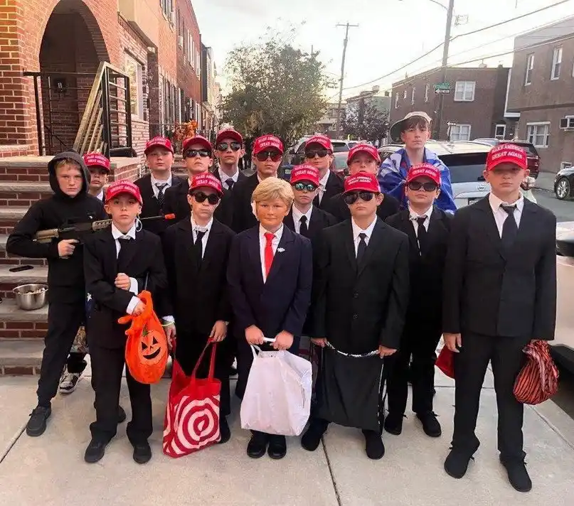 A group of children dressed in black suits, wearing red 'make america great again' hats and sunglasses, posing for a photo…