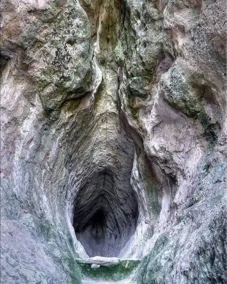 a natural rock formation resembling a human face with a nose and mouth, carved into a cliffside, with overlaid text reading…