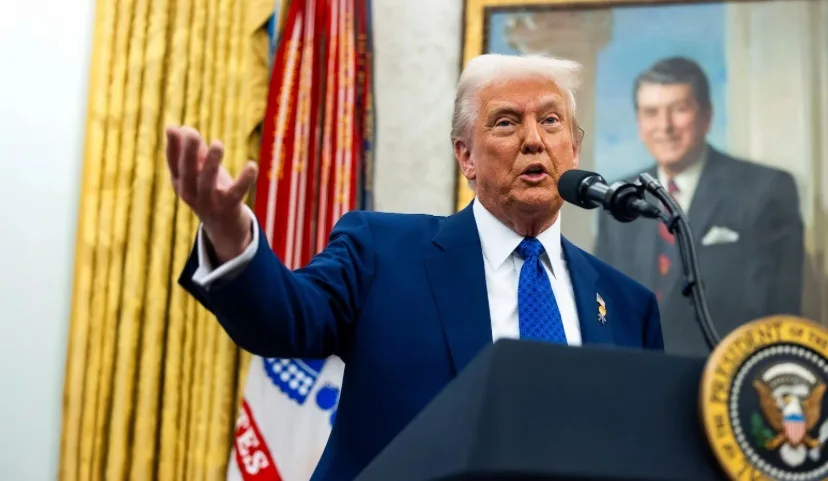 A man in a blue suit and tie stands at a podium with the presidential seal, gesturing with his right hand while speaking…