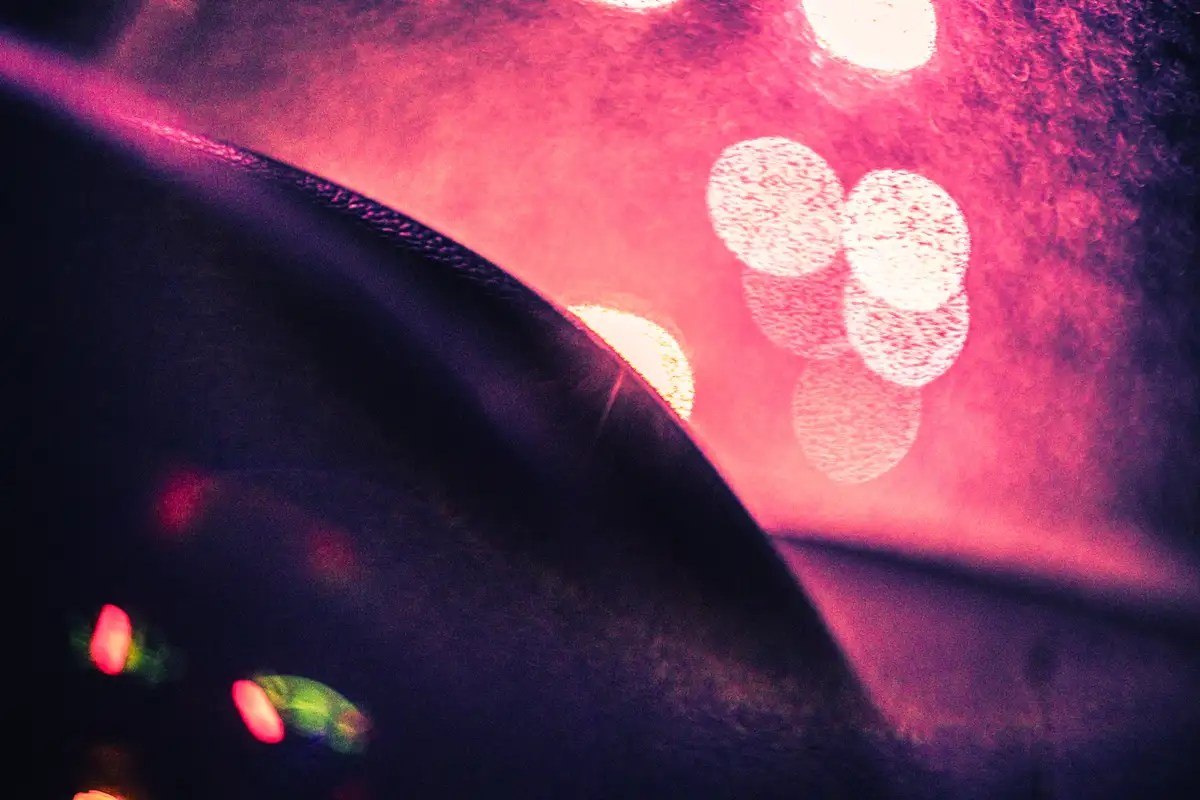 An abstract photo of blurred, colorful lights against a dark, textured surface, with a diagonal dark shape cutting across…