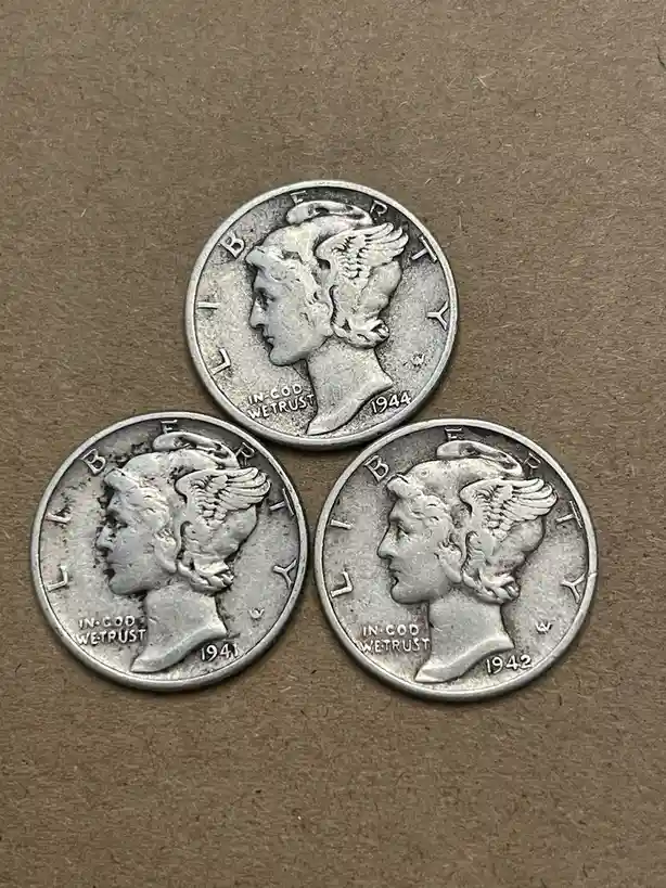Three silver Mercury dimes from 1941, 1942, and 1944 are arranged in a triangle on a brown surface. Each coin shows the…