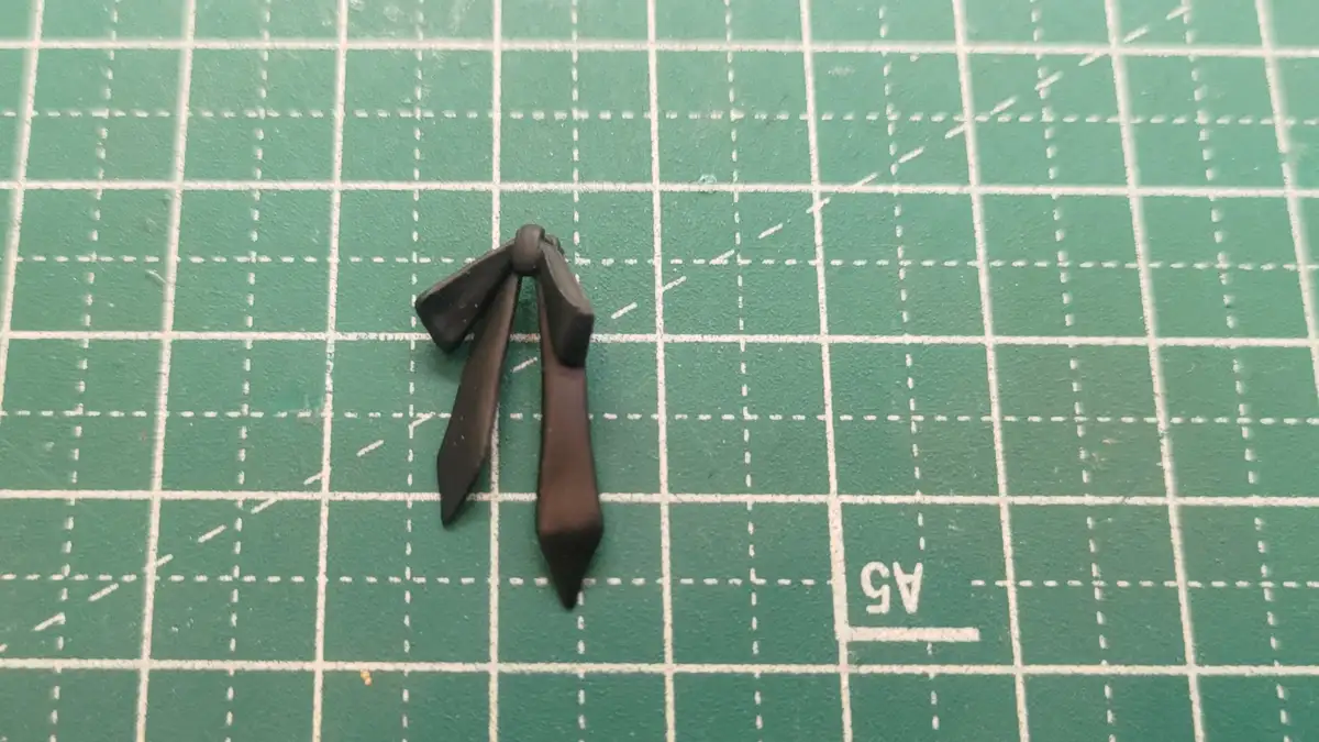 A small, dark brown clay bowtie sits centered on a green self-healing cutting mat with white grid lines and dashed…