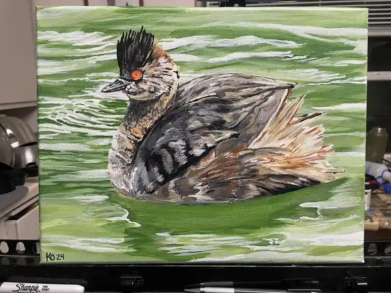 A painting of a bird with a black crest, orange eye, and grey-brown feathers floating on green water with white ripples. The…