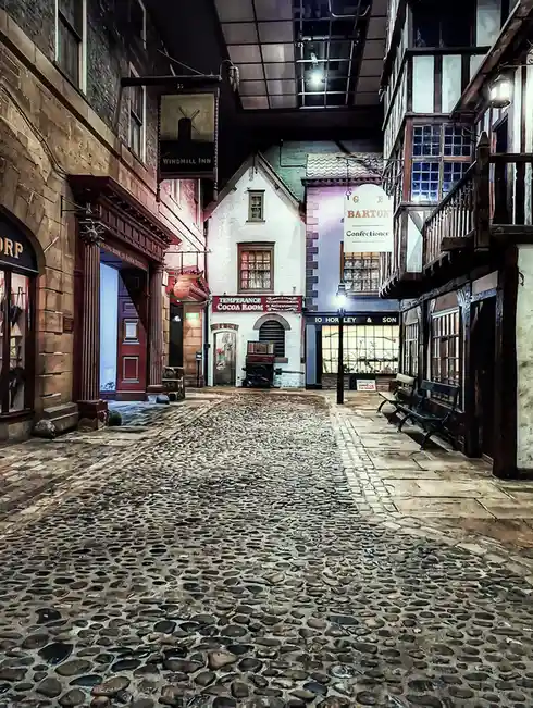 A cobblestone street lined with historic-style buildings, including a 'Windmill Inn', 'Temperance Cocoa Room', and 'G E…