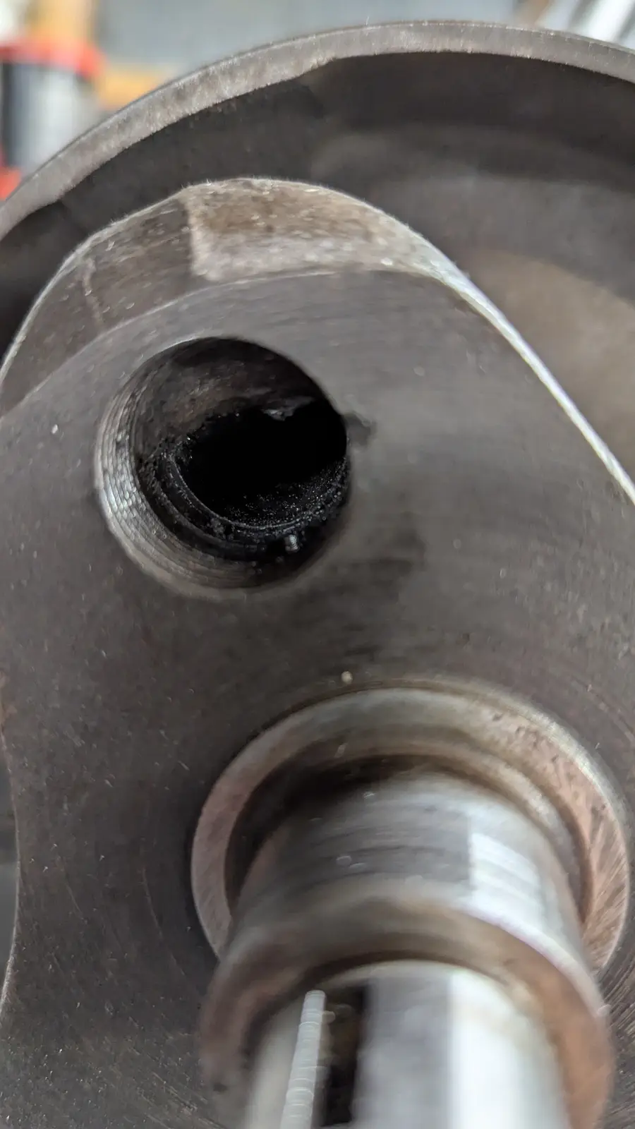 A close-up photo shows a dark, circular hole in a worn, metallic mechanical part, with another cylindrical component…