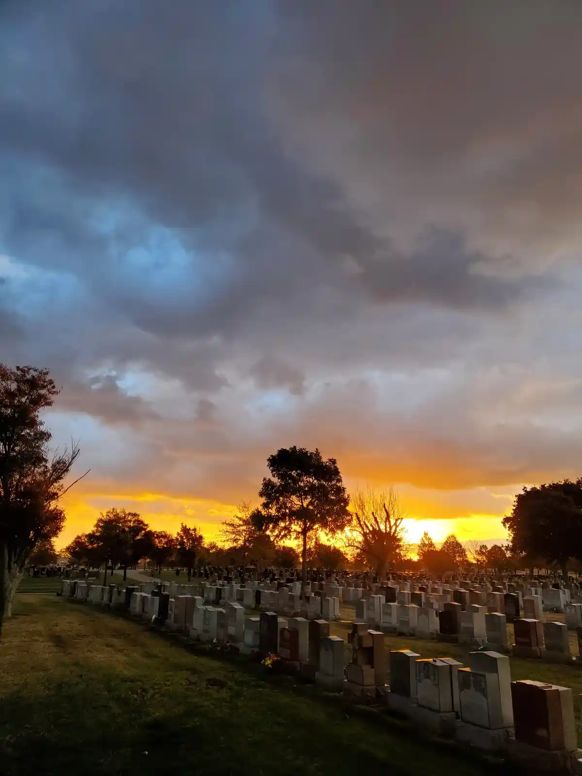 A cemetery at sunset with rows of gravestones under a dramatic sky of orange and dark clouds. The overlaid text reads 'i'm…