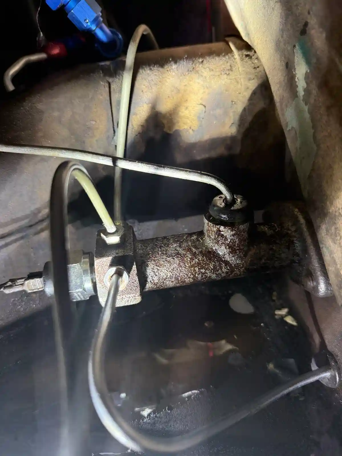 A close-up photo shows a rusty, corroded brake master cylinder inside a vehicle's engine bay, with wires and hoses…