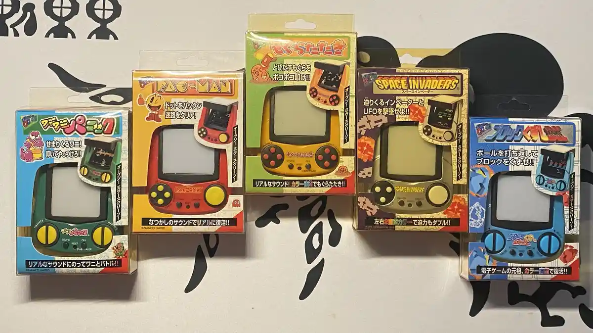 Five retro handheld game consoles in their original Japanese packaging are displayed side-by-side on a white surface with…