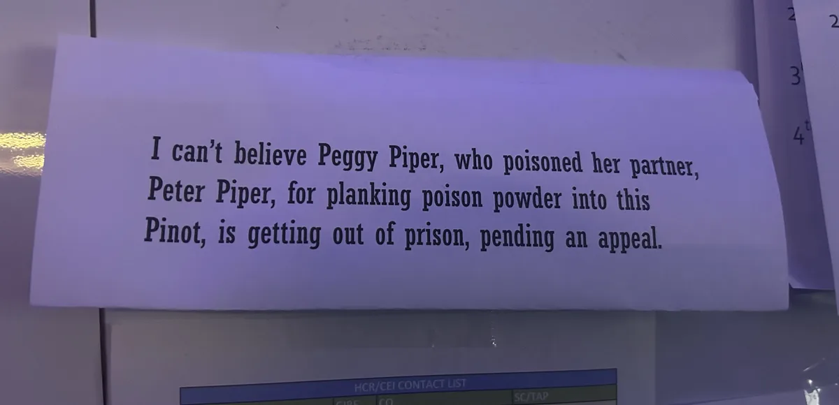 A piece of paper with black text is taped to a surface, likely a wall or board, under dim purple lighting. The text…