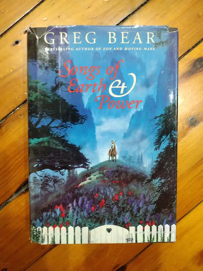 A physical copy of Greg Bear's book 'Songs of Earth & Power' rests on a wooden floor. The cover art depicts a lone rider on…