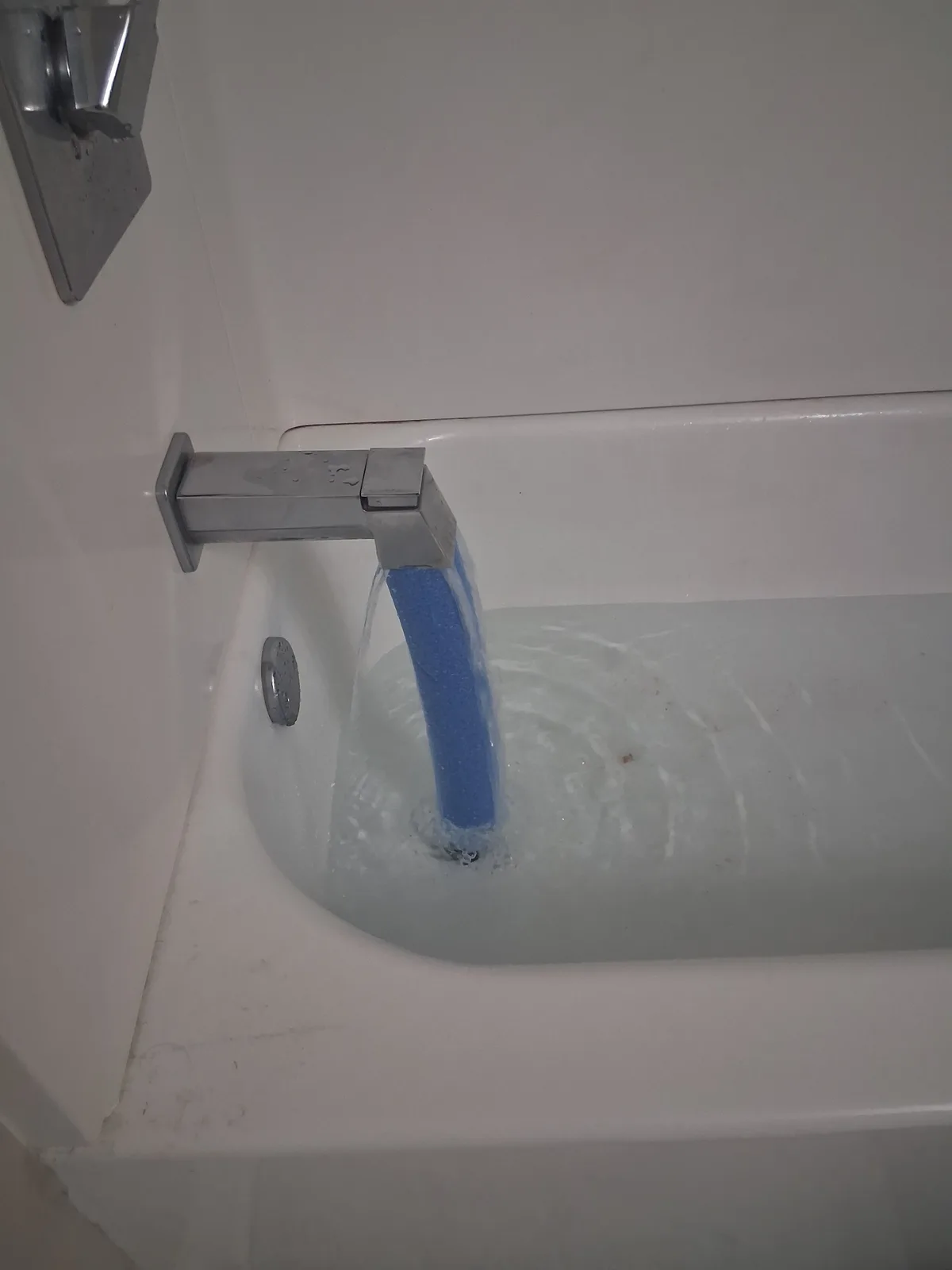 A close-up photo shows water flowing from a modern silver bathtub faucet into a white tub, but the stream is visibly…
