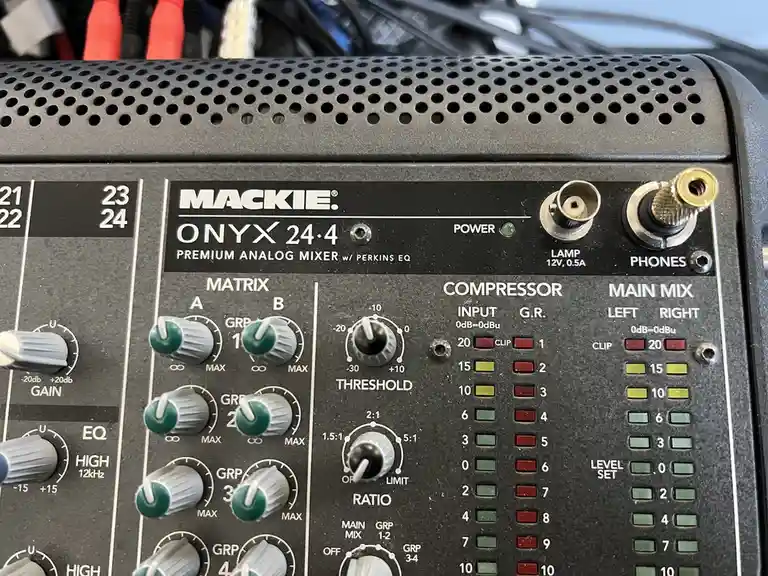A close-up photo of a Mackie Onyx 24.4 premium analog audio mixer, showing its control knobs, buttons, and level meters. The…
