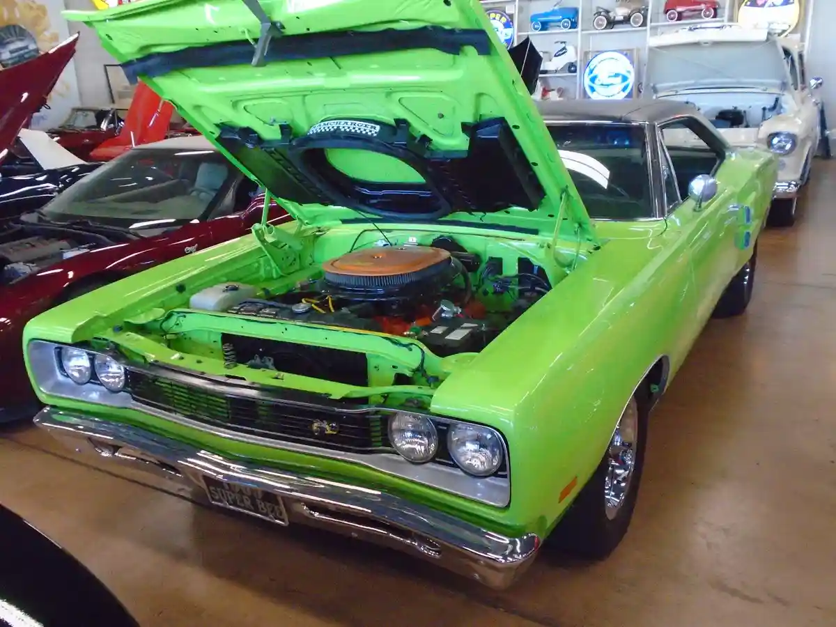 A bright lime-green 1970 Dodge Super Bee muscle car with its hood open, revealing a detailed engine bay, is parked indoors…