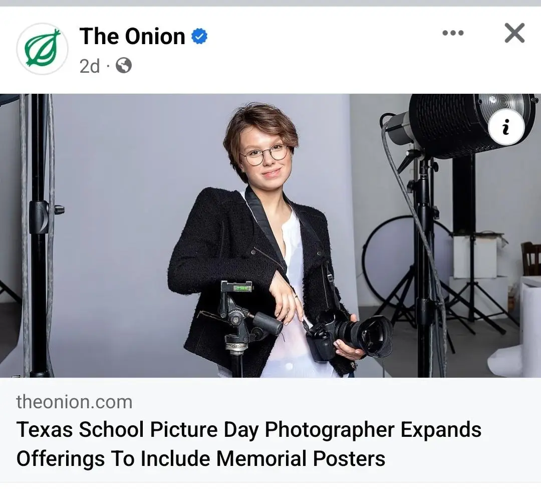 A woman with short hair and glasses, wearing a black jacket over a white shirt, stands in a photo studio holding a camera…