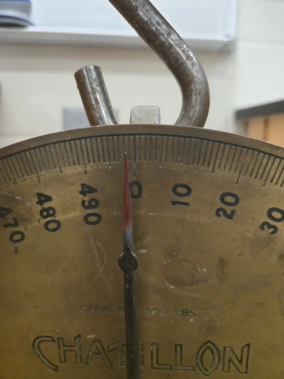 A close-up of an old, brass Chatillon scale with a needle pointing exactly at the '0' mark on its 470-500 lbs capacity dial…