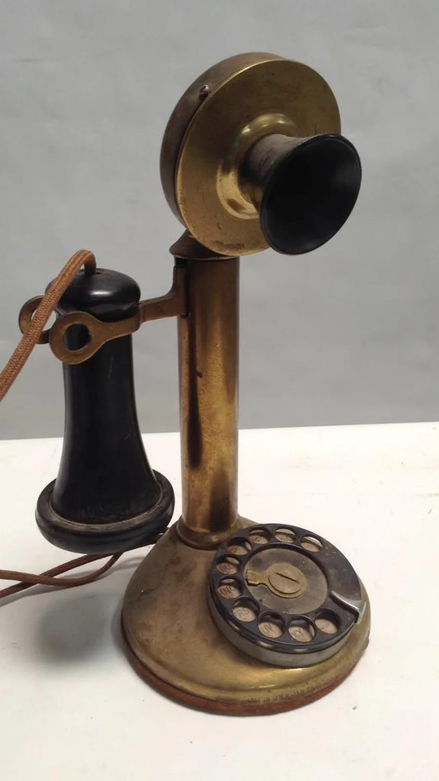 A vintage brass rotary telephone with a black handset and receiver, sitting on a white surface. The overlaid text reads…