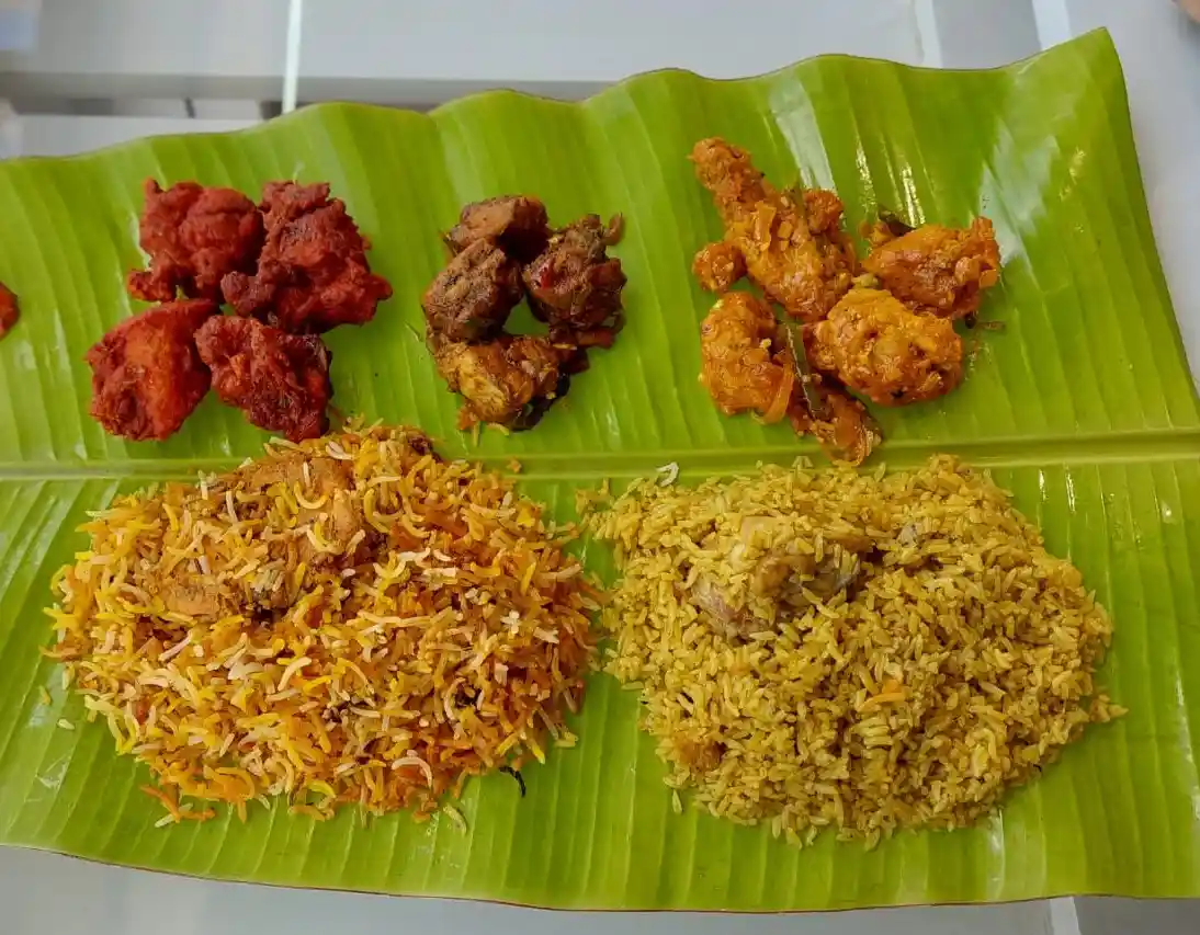 a large green banana leaf holds two portions of rice and three types of fried chicken, arranged in sections. overlaid text…